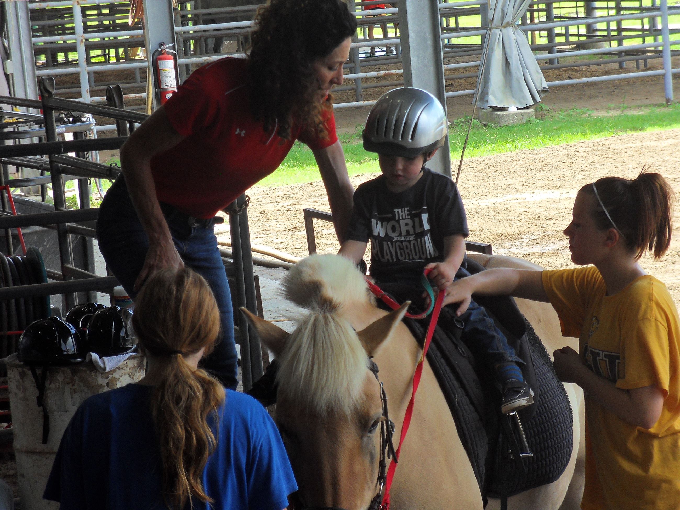 Woman helping a child onto a horse