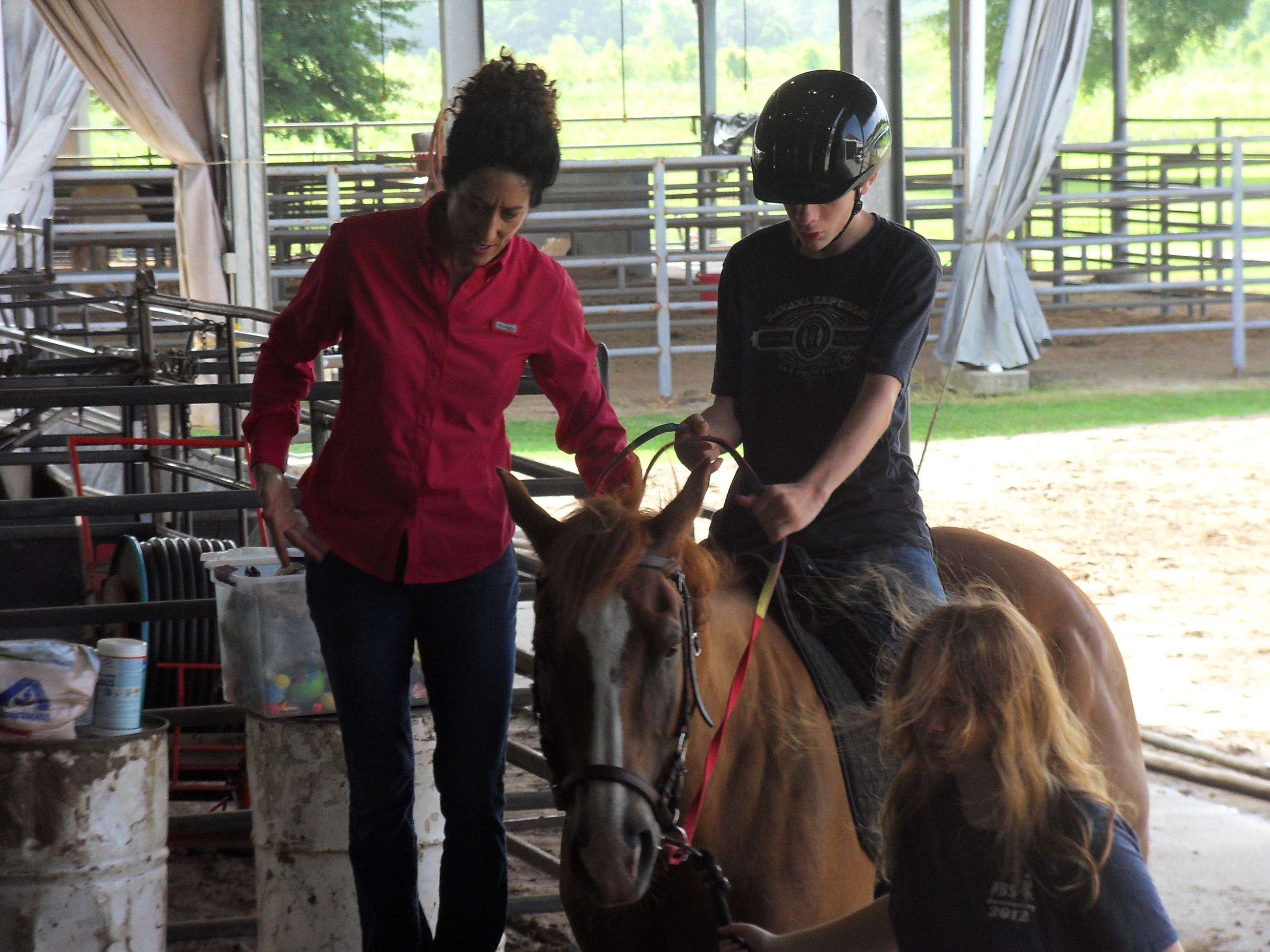 Boy riding a horse with a woman assisting him